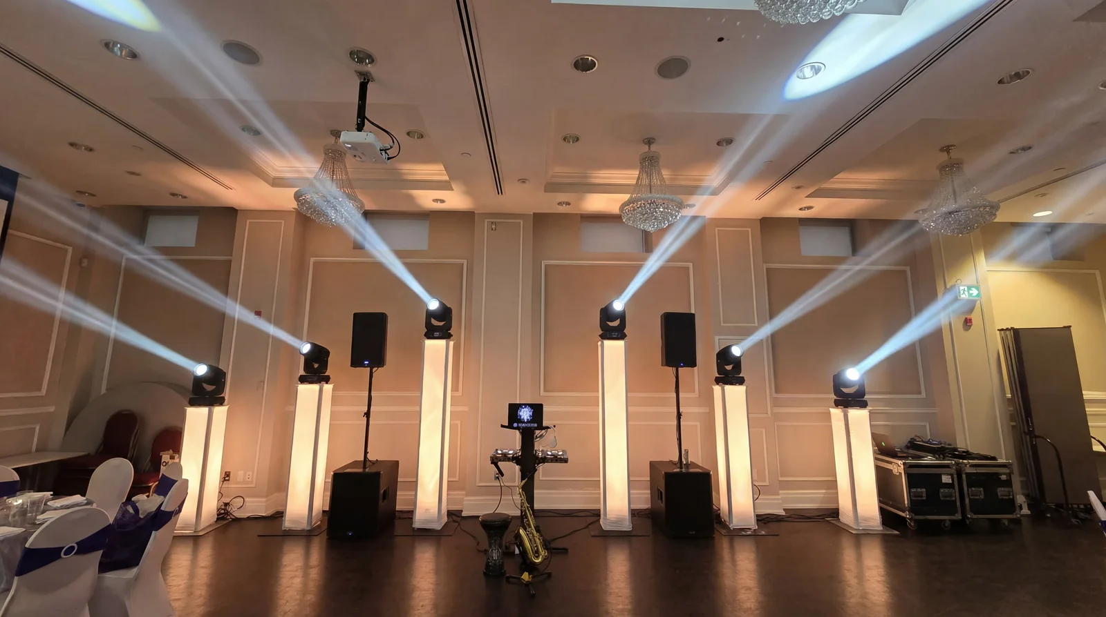Six illuminated truss totems with moving heads flanking a DJ booth in a hotel ballroom